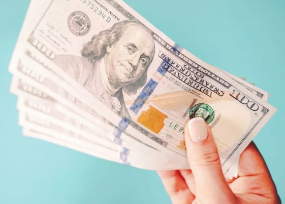 Woman's hand holding $100 bills on a blue background