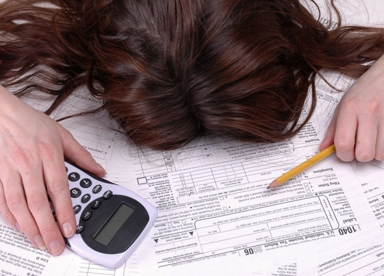 Woman with head on tax documents, holding a calculator and pencil