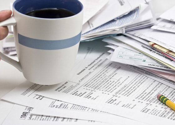 Tax forms sitting on a table and a person picking up a coffee mug