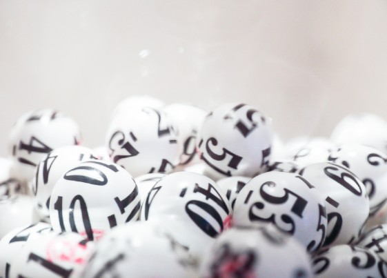 Many white lottery balls with black numbers on them are close together. Close up shot is taken against a white background.